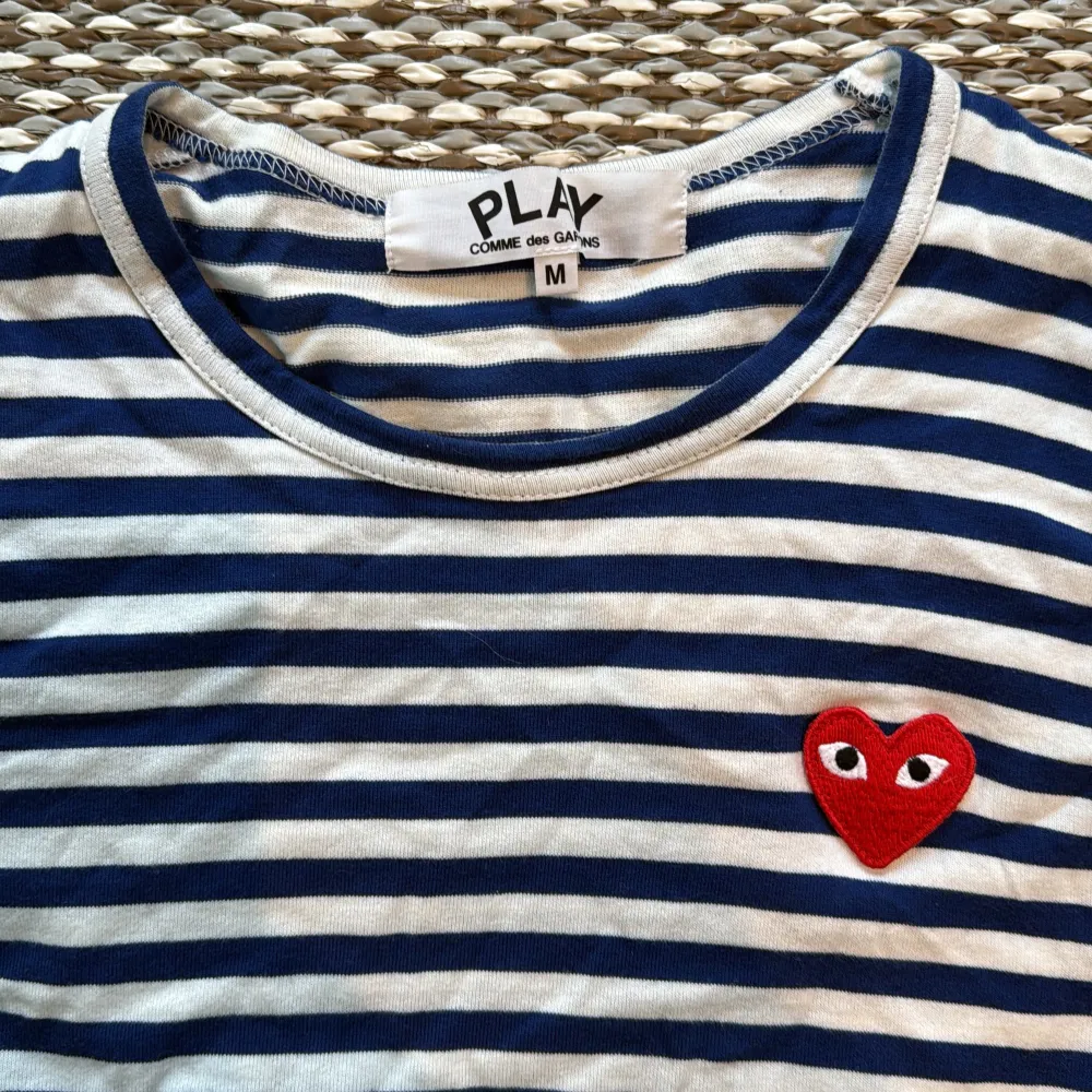 Säljer en randig tröja från Comme des Garçons med blå och vita ränder. Tröjan har ett rött hjärta med ögon på bröstet och långa ärmar. Perfekt för en stilren look! . Neuletakit & Villapaidat.