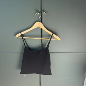 Svart ärmlös linnetopp - Snygg svart linnetopp med smala axelband. Perfekt för varma dagar eller som lager under en jacka. Enkel och stilren design som passar till det mesta.