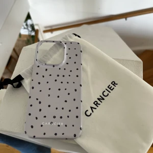 Prickigt mobilskal från Carncier IPhone 15 PRO - Lyxigt mobilskal från Carncier med ett stilrent prickigt mönster i svart och vitt. Skalet kommer med en praktisk tygpåse för förvaring. Perfekt för att ge din mobil en personlig touch! 
