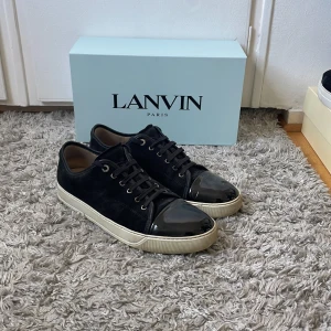 Svarta sneakers från Lanvin - Säljer dessa stilrena svarta sneakers från Lanvin i storlek 46, glansig tå och klassisk snörning. Skorna är i fint skick och kommer självklart med originalbox, dustbag samt extra skosnören. Nypris ca 4000 kr – passa på att fynda! Skicka gärna ett meddelande vid frågor eller om du vill se fler bilder.