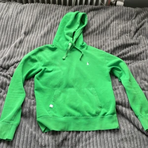 Grön hoodie från Ralph Lauren - Säljer en snygg grön hoodie från Ralph Lauren med klassisk känguruficka och justerbar huva. Den har en broderad logga på bröstet i vitt. Perfekt för en avslappnad stil.