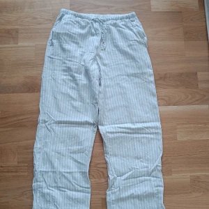Randiga linne sommar byxor  - Säljer ett par bekväma och randiga byxor från Gina Tricot i storlek  146/152. Byxorna är vita med grå ränder och har en elastisk midja med snörning för extra komfort. Perfekta för sommaren!