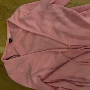 Rosa ribbad kofta från H&M - Säljer en söt rosa ribbad kofta från H&M. Den har långa ärmar och en knytning framtill. Perfekt för att lägga till en färgklick i garderoben. Passar bra till både jeans och kjol.