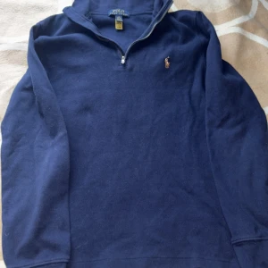Mörkblå tröja från Polo Ralph Lauren - Säljer en snygg mörkblå tröja från Polo Ralph Lauren med dragkedja vid halsen och det klassiska broderade logotypen på bröstet. Perfekt för en stilren look.