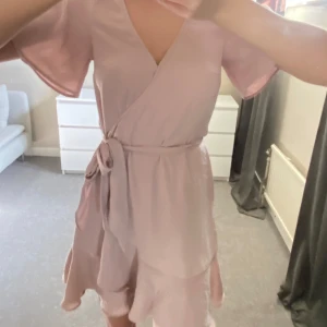 Ljusrosa omlottklänning - Säljer en söt ljusrosa omlottklänning med korta ärmar och knytband i midjan. 