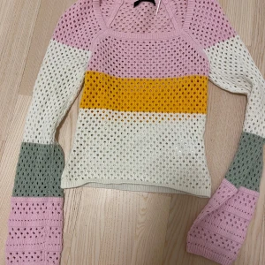 Flerfärgad stickad tröja från BikBok - Säljer en snygg flerfärgad stickad tröja från BikBok i storlek XS. Tröjan har ett hålmönster och är randig i rosa, gul, vit och grön. Den har långa ärmar och en bekväm passform.