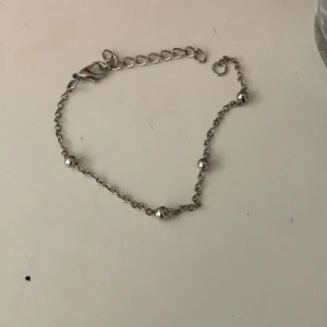 Fyra olika armband - Säljer fyra olika armband: ett silverfärgat kedjearmband med små kulor, ett pärlarmband i vitt, blått och guld, ett rosa elastiskt armband och ett smalt silverfärgat armband med lås. Perfekta accessoarer för att komplettera din stil.