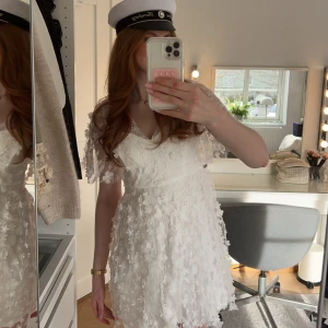 Vit studentklänning - Studentklänning ifrån Bubbleroom i nyskick, endast testad. Nypris 999kr. Klänningen har ett blommigt mönster med korta ärmar och en v-ringad design. Säljer då jag redan har en studentklänning!