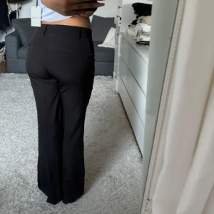 Svarta kostymbyxor - Snygga svarta kostymbyxor med låg midja och bootcut-stil. Byxorna har en klassisk design med dragkedja framtill. Perfekta för en stilren look.