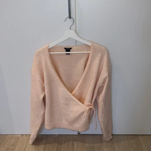  omlottkofta från Lindex - Säljer en mysig rosa/peach färgad omlottkofta från Lindex. Koftan är använd fåtal gånger men är lite nopprig på vissa ställen. 