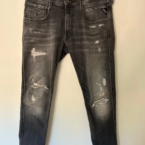 Grå jeans från Replay - Snygga grå jeans från Replay med slitna detaljer och en klassisk femficksdesign. Jeansen har en knappgylf och är tillverkade i ett bekvämt denimtyg. Perfekta för en avslappnad stil.