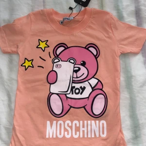 Moschino barn t-shirt - Säljer en söt t-shirt för barn från Moschino med en rosa nalle. Oanvänd helt ny i storlek 95, passade inte min brorsa så därför jag säljer den. 