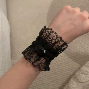 Svart spetsarmband med pärlor - Elegant svart armband i spets med dekorativa svarta pärlor. Armbandet har en romantisk känsla med sina spetsdetaljer och är perfekt för att ge en extra touch till din outfit.