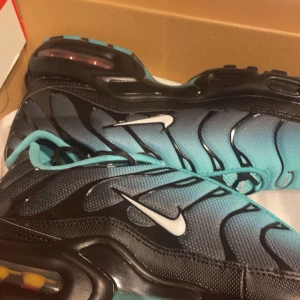 Nike Air Max Plus i svart och turkos - Snygga Nike Air Max Plus sneakers i en cool kombination av svart och turkos. Skorna har den ikoniska vågdesignen och en synlig Air Max-dämpning i sulan för extra komfort. Perfekta för både stil och funktion. OBS Bilden är tagen när skorna var nya, vill man ha ytterligare bilder hur skorna ser ut nu kan man kontakta mig för bilder. 