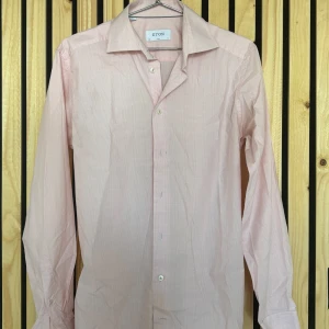 Ny Eton skjorta  - Säljer en stilren rosa skjorta från Eton i storlek 38. Helt ny utan prislapp. Skjortan har ett diskret rutmönster och är tillverkad i 100% bomull. Den har en slim passform och långa ärmar med knappar framtill. Perfekt för en elegant look.