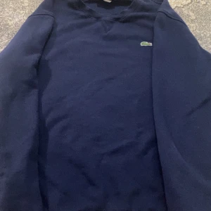 Lacoste sweatshirt - Mörkblå sweatshirt från Lacoste med klassisk krokodillogga. Storleken är S men passar även M, Bra skick, 1•1