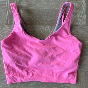 Rosa croppad linnetopp sport - Snygg croppad linnetopp i stark rosa färg med breda axelband. Perfekt för varma dagar eller som ett lager under en skjorta. Mjuk och stretchig bomullskänsla som sitter skönt mot kroppen.