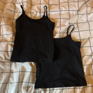 Svarta linnen från H&M, 2-pack - Två svarta linnen från H&M med smala axelband och enkel, rak passform. Perfekta att ha under en hoodie eller bara som de är. Mjukt material som känns skönt mot huden och passar till allt. Dom är i stl 134/140 men passar även mig med stl 146/152 då dom bara sitter lite tajtare. Använda väldigt fåtal gånger då jag skulle köpt en lite större storlek.