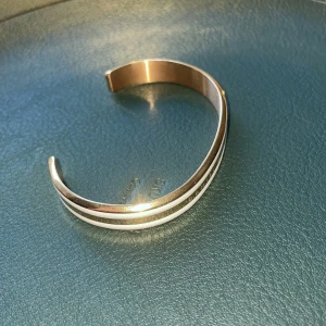 Roséguldfärgat armband Daniel Wellington - Snyggt armband i roséguld från Daniel Wellington med en stilren, öppen design. Armbandet har en vit rand längs kanten som ger en modern touch. Perfekt accessoar för dig som gillar minimalistisk och trendig stil.