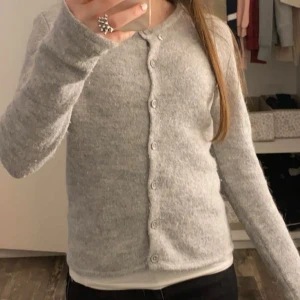 Ljusgrå stickad kofta med knappar - Mysig ljusgrå stickad kofta med rund hals och knäppning hela vägen fram. Koftan har långa ärmar och en enkel, clean look som passar till allt. Perfekt att slänga på sig när det är lite kyligt ute. (Vi kan diskutera om priset också)🫶