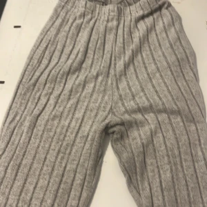 Grå ribbade utsvängda byxor  från SHEIN - Mysiga grå utsvängda byxor  från SHEIN i storlek XS. Byxorna har ribbat mönster, elastisk midja och är tillverkade i ett mjukt, stickat material. Perfekta för chill dagar hemma eller när du vill vara extra bekväm.
