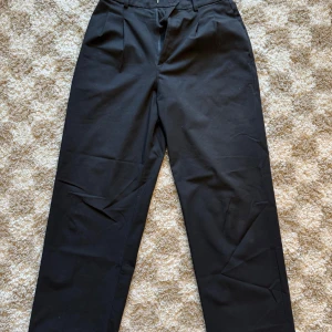 Svarta kostymbyxor från Uniqlo - Svarta oversized kostymbyxor från Uniqlo i storlek S. Dessa är dammodell och har en rak / loose passform med hög midja och hällor för bälte. Materialet är en mix av polyester, viskos och elastan = mjuka och något elastiska. Tror dessa har utgått ur deras sortiment så passa på!