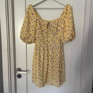 Gul blommig kortklänning från BikBok - Supersöt gul kortklänning från BikBok med lila och rosa blommor. Klänningen är aldrig använd💛