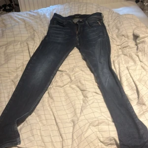 Replay jeans i mörkblå denim - Snygga mörkblå jeans från Replay med klassisk femficksdesign och diskreta slitningar. Modellen har smal passform och raka ben, med detaljerade bakfickor och dragkedja fram. Perfekta för dig som gillar stilrena och bekväma jeans. Skickas helst med instabox