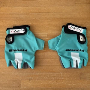 Bianchi cykelhandskar Nalini S - Snygga fingerlösa cykelhandskar från Bianchi x Nalini i turkos och grått med svart och vit detalj. Kardborreknäppning och vadderad insida för extra komfort. Perfekta för dig som vill ha stil och funktion på cykelturen.