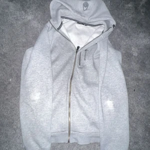 Ljusgrå hoodie från Didriksons - Säljer en ljusgrå hoodie från Didriksons med dragkedja framtill och huva. Tröjan har långa ärmar och är tillverkad i mjuk bomullsblandning. Perfekt för chill dagar eller när du vill ha en enkel och clean look.