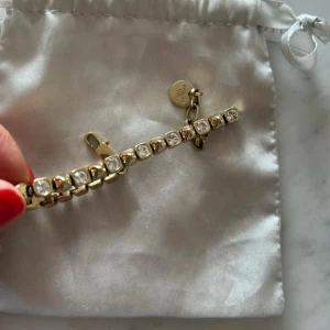 Guldarmband med glittrande stenar från Dyrberg Kern /Kern - Snyggt guldarmband från Dyrberg/Kern med glittrande, runda stenar infattade i varje länk. Armbandet har en klassisk och lyxig känsla med justerbar kedja och liten rund bricka med logga. Perfekt för dig som gillar statement-smycken med extra bling.