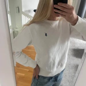 Vit sweatshirt från Polo Ralph Lauren - Vit sweatshirt från Polo Ralph Lauren med klassisk blå broderad logga på bröstet. Tröjan har rund hals, ribbade muddar och är i mjuk bomull. Perfekt basic tröja med snygg passform. Använd fåtal gånger, inga fläckar eller tecken på användning. Nypris 2095kr. 
