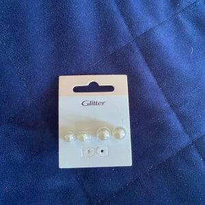 Pärlörhängen från Glitter - Två par klassiska pärlörhängen i olika storlekar från Glitter. Örhängena är vita och har en rund form, perfekta för att ge en elegant touch till din stil.