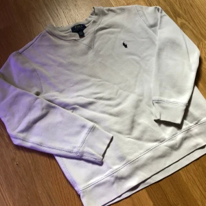 Vit sweatshirt från Polo Ralph Lauren - Klassisk vit sweatshirt från Polo Ralph Lauren med broderad marinblå logga på bröstet. Tröjan har rund halsringning, långa ärmar och ribbade muddar. Tillverkad i mjuk bomull som är skön att ha på sig hela dagen.