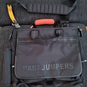 Svart crossbody från Parajumpers - Snygg svart datorväska från Parajumpers med orange handtag, gula detaljer och robust axelrem. Väskan har stora loggan framtill, orange sömmar och coolt spänne i metall. Tillverkad i slitstark polyester med flera fack och dragkedjor för smart förvaring.ny med kvitto 