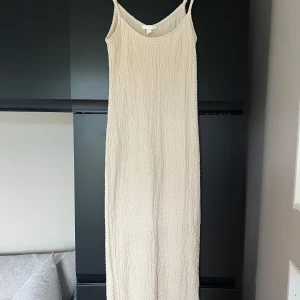 Lång beige klänning med smala axelband - Lång, ljusbeige klänning med smala axelband. Klänningen är i stretch och passar de flesta beroende på hur man vill att den ska sitta. Använd en gång. Fin till stranden och dylikt. Köparen står för frakten 💕