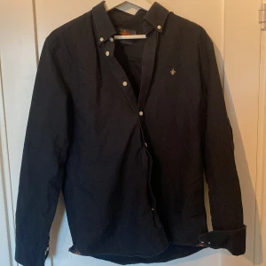 Svart skjorta från Morris, storlek M - Svart skjorta från Morris i storlek M med klassisk krage och vita knappar. Perfekt för klassisk look och fest stil. Säljer den här stilrena Morris skjortan då den inte passar mig längre har vuxit ur den! Ny pris 1299kr säljer den för 350kr tveka inte på att höra av er. 