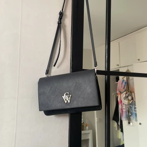 Svart axelväska  - Snygg svart axelväska. Väskan har justerbar axelrem och är tillverkad i slätt skinnimitation. Perfekt storlek för mobil, plånbok och andra essentials.