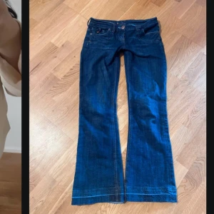 Mörkblå vintage lågmidjade bootcut jeans med broderi - Snygga mörkblå vintage jeans med bootcut passform och dekorativa broderier på bakfickorna. Jeansen har låg midja, low waist, Low Rise.Materialet är denim. Jeansen är i jättebra skick, använt fåtal gånger. 