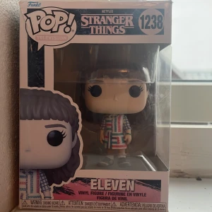Eleven (Stranger Things) Pop! Television #1238 - Cool Funko Pop! figur av Eleven från Stranger Things. Perfekt för fans av serien som vill ha en unik samlarpryl på hyllan. Eleven bär sin ikoniska färgglada klänning och har detaljerad design. Ett måste för dig som älskar popkultur och Netflix-serier!