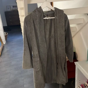 Grå badrock från Calvin Klein L - Mjuk och skön grå badrock från Calvin Klein i frotté med huva, stora fickor och bälte i midjan. Snygg logga på ärmen och insidan av kragen. Perfekt att chilla i efter duschen eller när du vill vara extra cozy hemma.