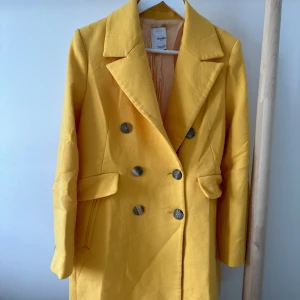 Gul kavaj från Mango, storlek M - Snygg gul kavaj från Mango med dubbelknäppning och klassisk krage. Jackan har två fickor med lock och knappar i mörk kontrast. Fodrad insida för extra komfort.