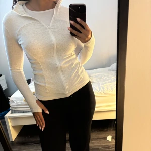 Vit ribbad zip-jacka med lång ärm - Slimmad vit jacka med ribbad struktur och hel dragkedja framtill. Långärmad modell med hög krage och tumhål vid ärmslut. Perfekt för lager-på-lager och chill vardagsstil.