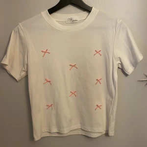 T-shirt med rosetter på - Söt T-shirt som inte e använd men rosa rosetter på!