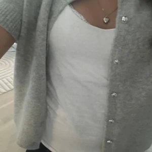 Ljusgrå kofta med silverknappar - Superfin ljusgrå kofta med korta ärmar och snygga silverknappar framtill. Koftan är stickad och har en mjuk, mysig känsla. Perfekt att slänga över ett linne för en chill och stilren look.