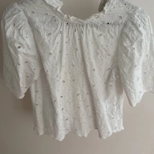 Vit blus - Superfin vit blus från Holly & Whyte i storlek XS. Blusen har broderade detaljer och hålmönster, puffiga korta ärmar och en söt volang vid halsen. Perfekt för en fräsch och romantisk look till sommaren eller våren.