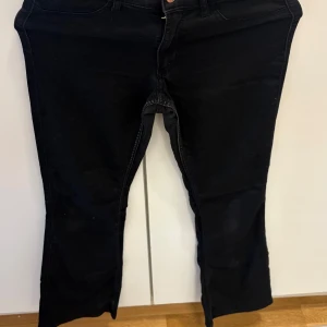 Svarta bootcut jeans från H&M - Svarta jeans från H&M med bootcut och låg midja. Byxorna har justerbar midja och flared ben, klassisk femficksmodell och är tillverkade i mjukt bomullstyg med lite stretch. Perfekta för dig som gillar en retro vibe och vill ha bekväma jeans med snygg passform.
