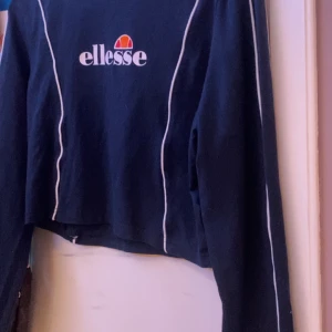 Mörkblå croppad tröja från Ellesse - Säljer en mörkblå croppad tröja från Ellesse med vita kontrastlinjer längs ärmarna och logga framtill. Tröjan har lång ärm och rund halsringning, perfekt för en sportig och avslappnad stil. Den är eu 44 men den är som en M/L.