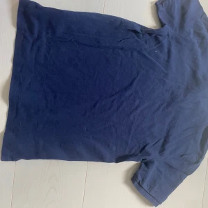 Marinblå pikétröja från Ralph Lauren - Snygg marinblå pikétröja från Polo Ralph Lauren med klassisk krage, två knappar och röd broderad logga på bröstet. Tillverkad i mjuk bomull, perfekt för en clean och stilren look.