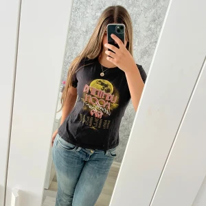 Svart Lightning Moon t-shirt  - Svart t-shirt med tryck framtill: stor gul måne och texten 'Lightning Moon World Tour 1979' i retrostil. T-shirten är i ekologisk bomull och har korta ärmar och rund hals. Perfekt för dig som gillar vintagevibbar. Vid frågor hör av dig!